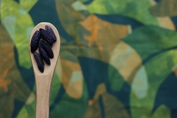 Tonka beans seed above a wooden spoon in a colorful background with green tones 