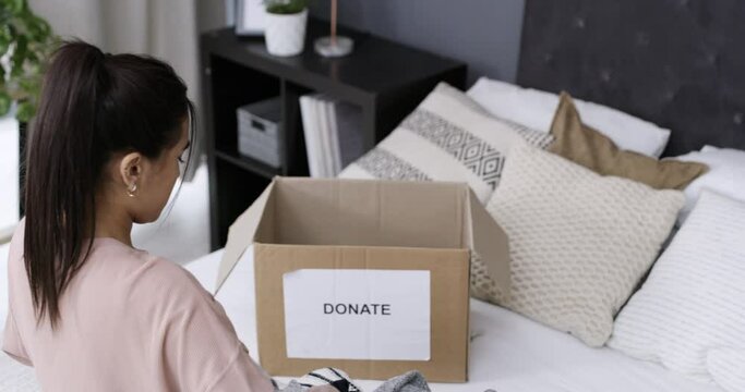 Woman, packing of clothes and donation for charity organisation and giving in kindness in bedroom. Person, humanity support or sorting of clothing in box, spring cleaning or generosity in above