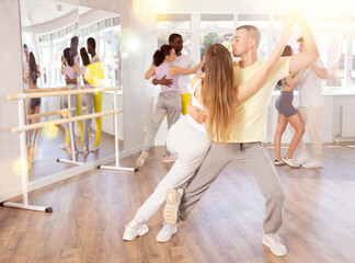 Positive young pair engaged in salsa dance together with other attendees of dancing courses