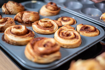 Freshly baked cinnamon rolls cooling in a muffin tin, with a golden cinnamon swirl visible, kitchen setting, delicious homemade desserts.