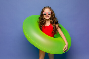 Funny happy child in red swimsuit and sun glasses smiling and holding a swimming ring on blue...