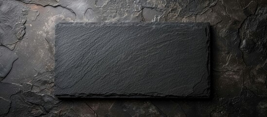 Black rectangular granite stone board on a black textured cement surface, seen from above with space for your text.