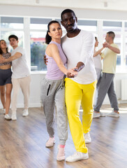 Graceful middle-aged pair training waltz dance poses together with other attendees of dancing...
