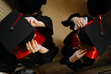 Two graduating girls in a black graduation cap with red tassels in a dress. graduates wear caps