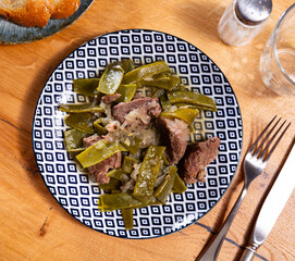 There is plate with braised beef fillet and stewed vegetable on wooden table. Stewed string beans...
