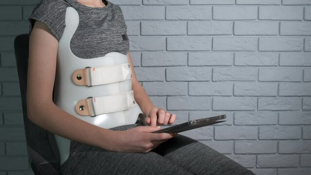 Mobility recovery in corset. A teen in Chenault corset sitting in the chair with laptop in the room.
