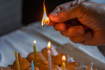 Men´s Hand holding matches and lighting colorful candles on the large homemade chocolate birthday...