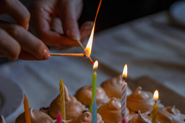 Hands of two people lighting colorful candles on the large homemade chocolate cake, decorated with...