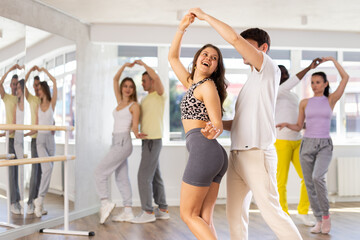 Slim young man and woman practicing tango dance in training hall during group dancing classes
