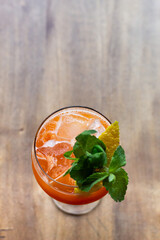 cocktail naranja en copa con hielo decorado con limon y menta en plano picado