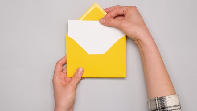 A hand pulls out a white card from a bright yellow envelope. Top view of a yellow envelope on gray background. Banner for social media ad with copy space