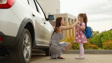 Young caring mother help little daughter putting on backpack going to primary school outdoor...