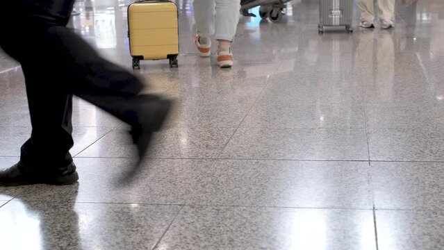 Woman rolling small yellow luggage bag on wheels at the airport rear view.