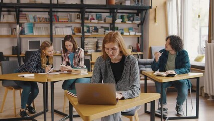 a group of students study and read books, write information in notebooks, on their phones and laptop in a library or classroom. Students in a good mood studying and reading books in the library - Powered by Adobe