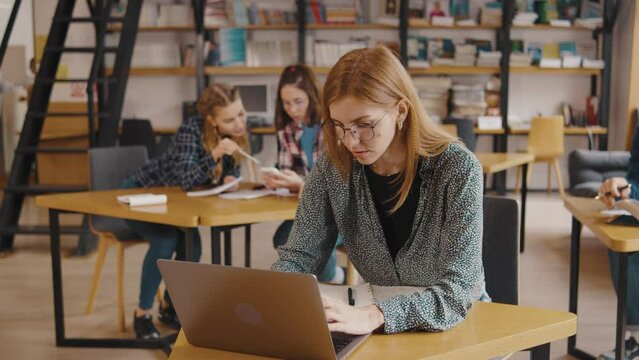 a group of students study and read books, write information in notebooks, on their phones and laptop in a library or classroom. Students in a good mood studying and reading books in the library