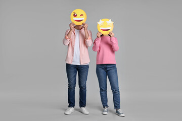 People covering faces with happy emoticons on grey background
