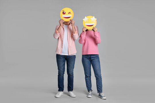 People covering faces with happy emoticons on grey background