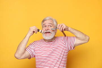 Senior man with mustache holding blade and brush on orange background