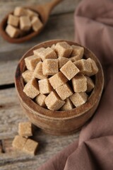 Brown sugar cubes in bowl on wooden table, closeup
