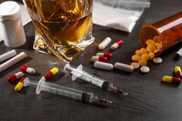 Alcohol and drug addiction. Whiskey in glass, syringes, pills and cigarettes on grey table, closeup