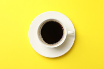 Cup of aromatic coffee on yellow background, top view