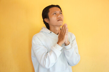 Handsome Asian young man wearing a hoodie praying with hands together asking for forgiveness