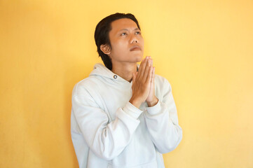 Handsome Asian young man wearing a hoodie praying with hands together asking for forgiveness