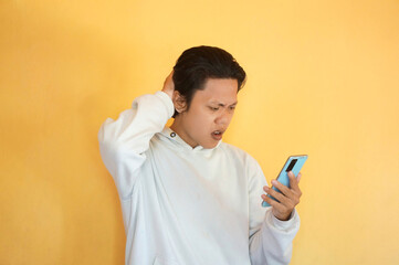 Fototapeta premium Asian young man showing confused facial expression while holding mobile phone