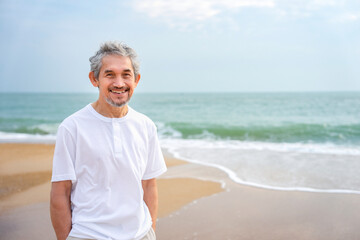 portrait happy asian senior man travel in nature,smiling and standing on the beach on summer time,concept of elderly pensioner lifestyle,holiday,travel,wellness,wellbeing