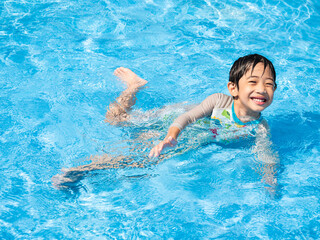 Happy Asian cute boy five years old is swimming and playing in the blue clear swimming pool. He is relaxing during his summer holidays.