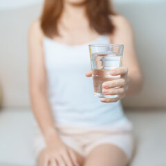 Happy woman holding water glass, female drinking pure water on sofa at home. Healthy, Refreshment,...