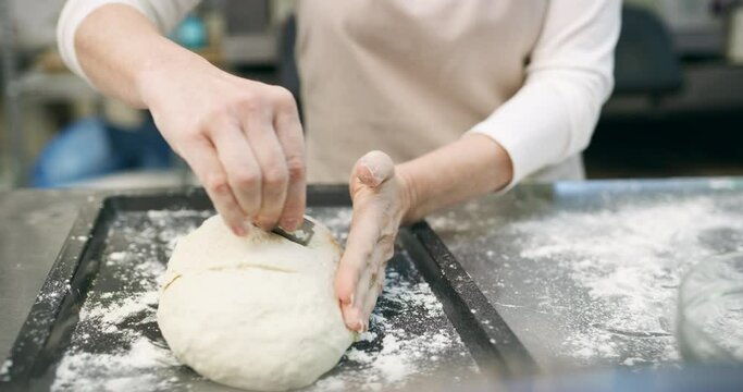 Chef, hands and blade on dough in bakery with production, process and handmade bread in restaurant or cafe. Woman, closeup and wheat in kitchen for service, culinary or pastry with sprinkle and oven