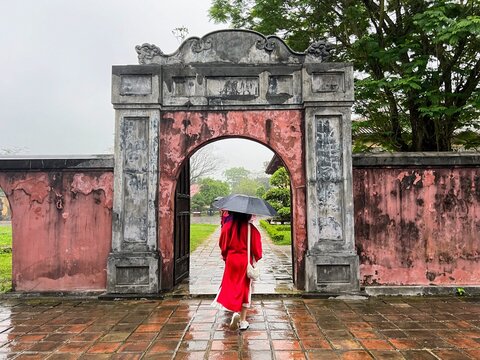 Asian girl holding an umbrella with back to camera dressed in traditional Vietnamese clothing in palace grounds