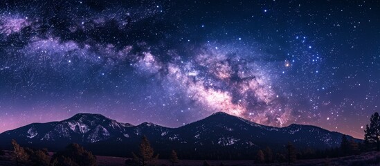 Scenic view of a dark night sky filled with shimmering stars and the Milky Way galaxy stretching above mountains in the background - obrazy, fototapety, plakaty