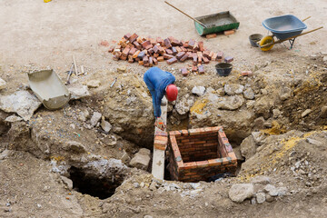 A man is working on a construction site, laying bricks in a hole