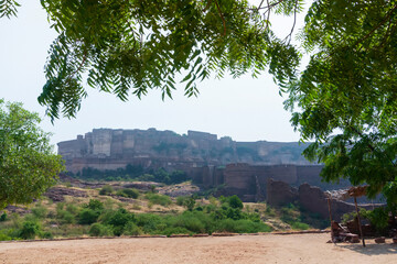 View of Mehrangarh fort from Rao Jodha desert rock park, Jodhpur, India. Green vegetation in the foreground and Mehrangarh fort in the background, with rocky landscape of the desert park.