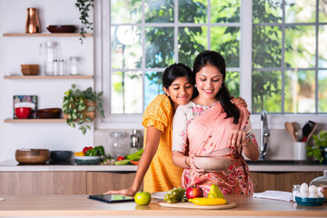Naklejka premium Indian mother daughter cooking in kitchen
