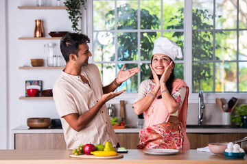 Asian indian married young couple sprinkling something on empty plate in the kitchen