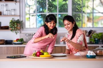Indian mother helping daughter making cake at home kitchen