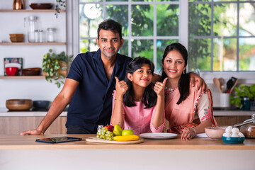 Cute little indian master chef with young parents in the kitchen making cake