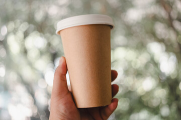 Hand holding one brown coffee paper cup with a lid. Mockup for your ad