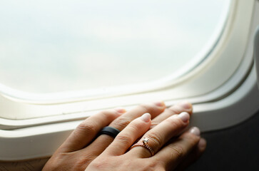 Close up of married couple's hands and wedding rings on airplane window while flying, romantic...
