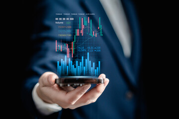 Businesswomen use smartphone to analyze virtual screens of graph stock market changes for trading,...