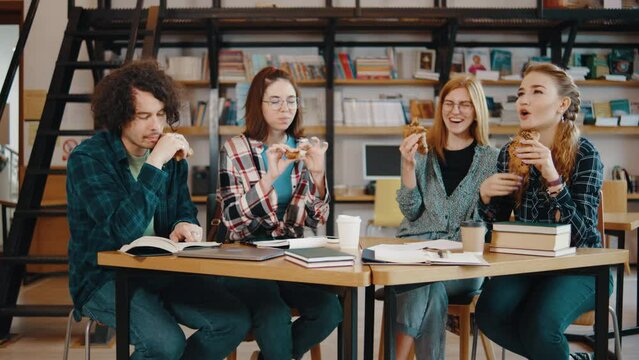 A group of students eat croissants in their free time from studying in a library or classroom. Students in a good mood studying and reading books in the library