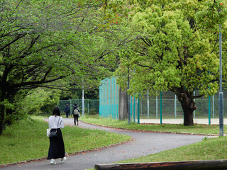春の公園の新緑と歩く人々の姿