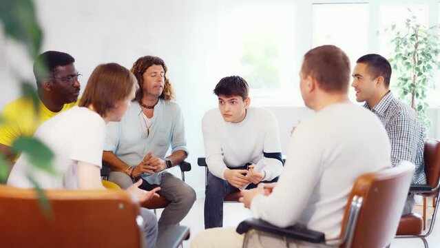 Cheerful carefree male colleagues of various ages and nationalities friendly talking sitting in circle on chairs in office lounge during break, sharing personal stories. High quality 4k footage
