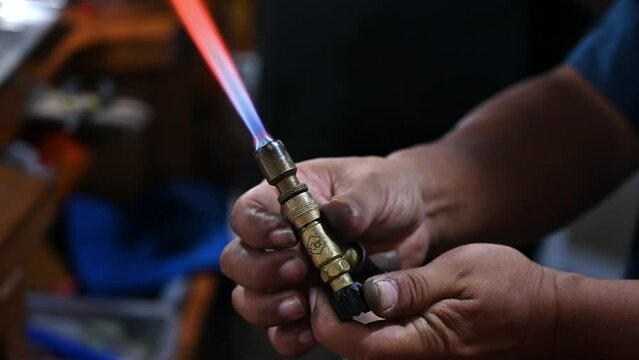 Close-up of a jeweler's hands working with a torch flame on a piece of jewelry in a workshop setting