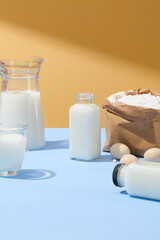 Against the light background, few eggs decorated with a paper bag of flour. Milk is filled inside some types of glass containers. Vacant space in the middle for product presentation
