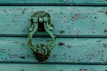 Antique metal handle, knocker with traces of rust on a wooden door, covered with peeling green paint