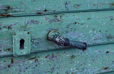 Antique brass handle on a wooden door covered with peeling green paint
